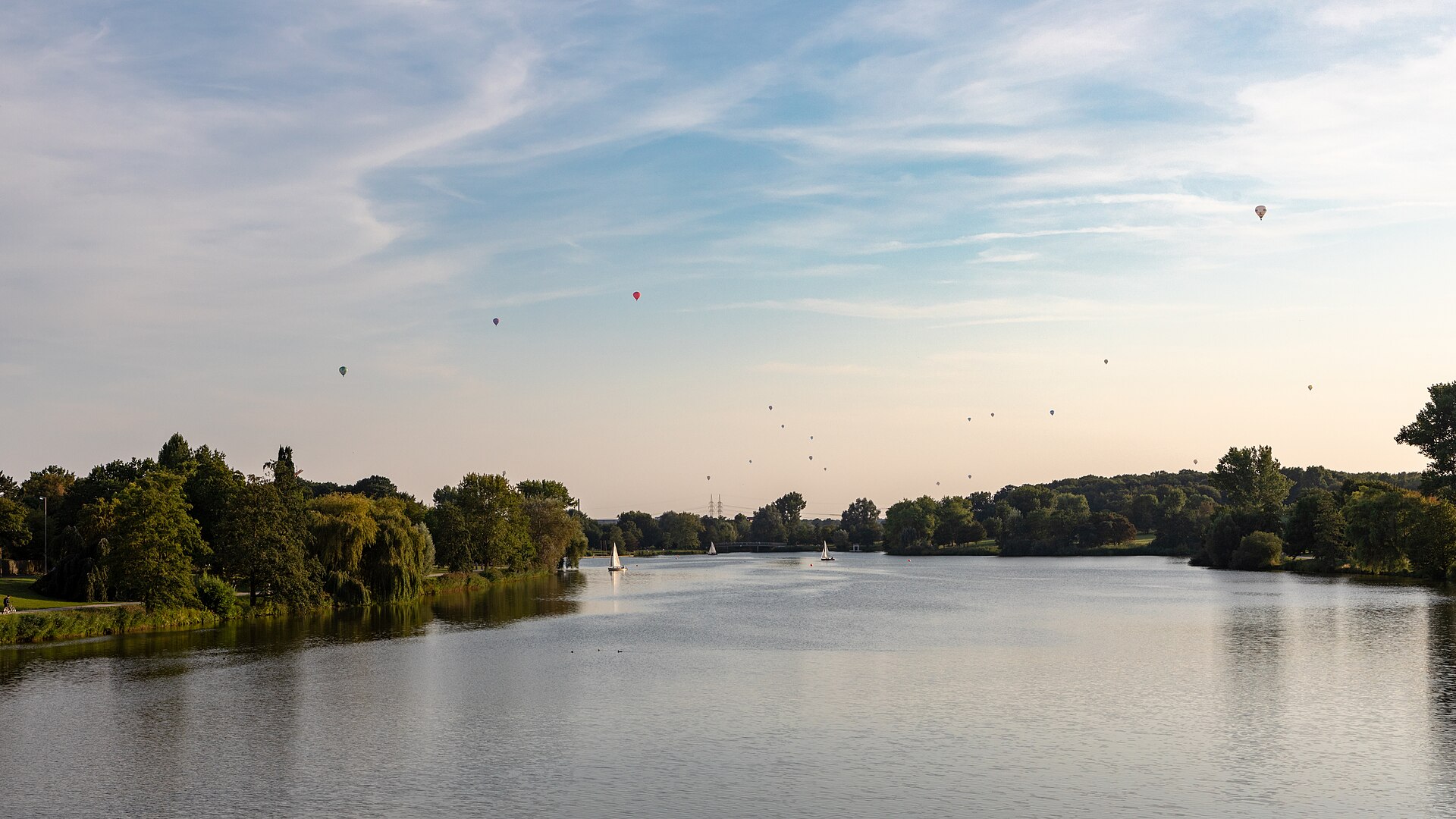 Hot air balloons rising over a lakeside town during a balloon festival