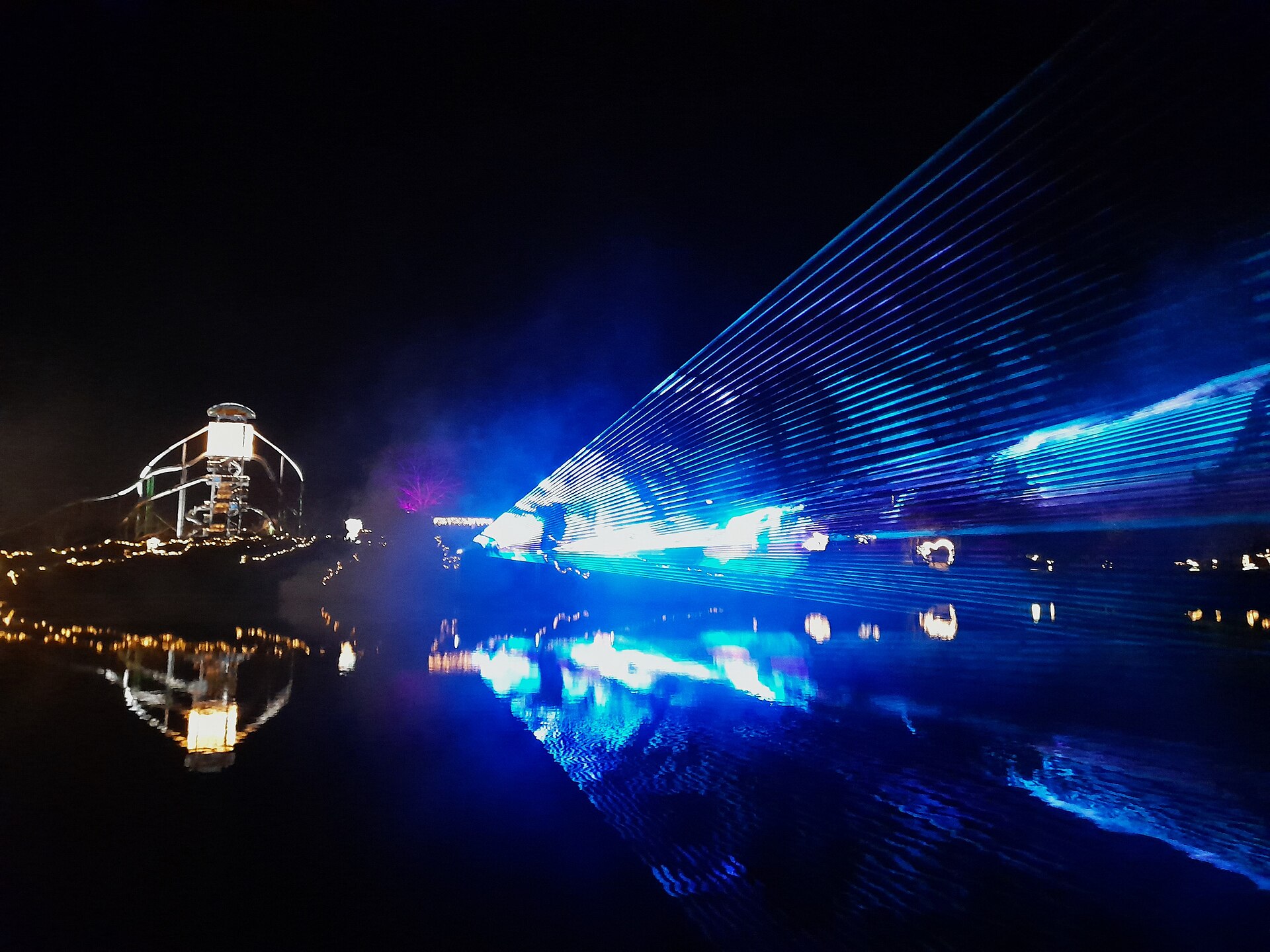 Blue laser beams fanning across the night sky over water